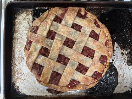 A lattice-top cherry pie, on a baking sheet partially covered with filling that overflowed and caramelized.