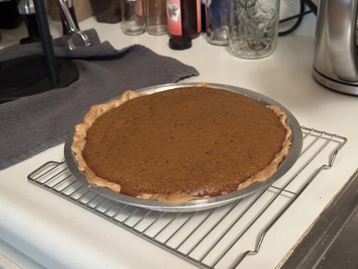 A pumpkin pie on a cooling rack on the counter, near the espresso maker.